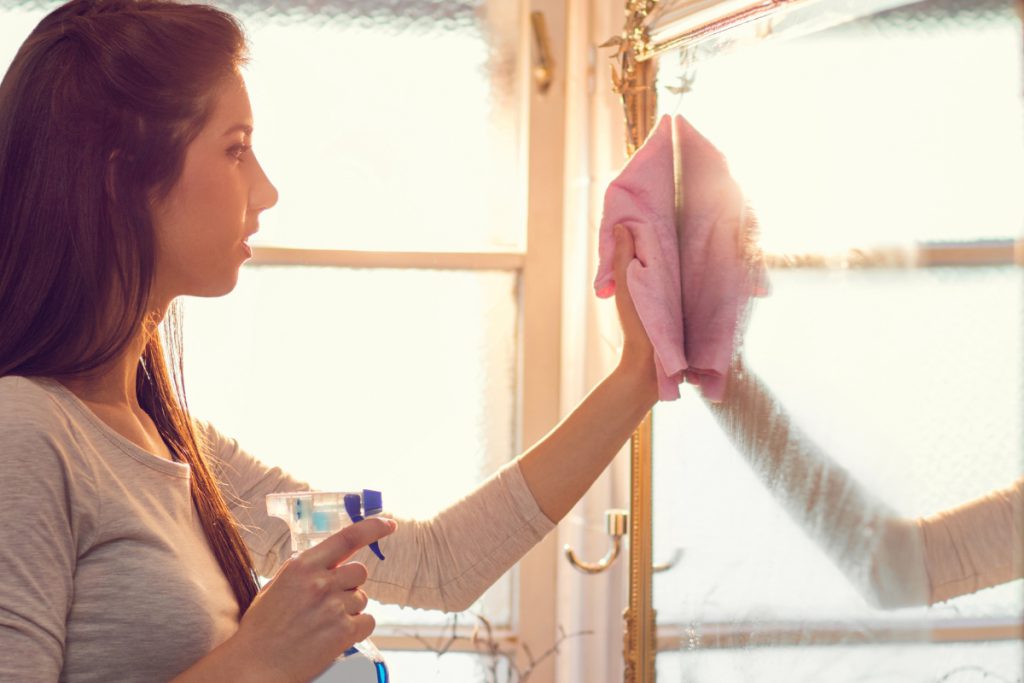 Woman cleaning her bathroom mirror with a microfiber towel