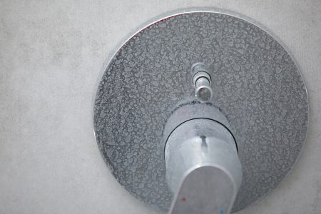 Limescale and soap scum on a close up of a shower faucet handle.