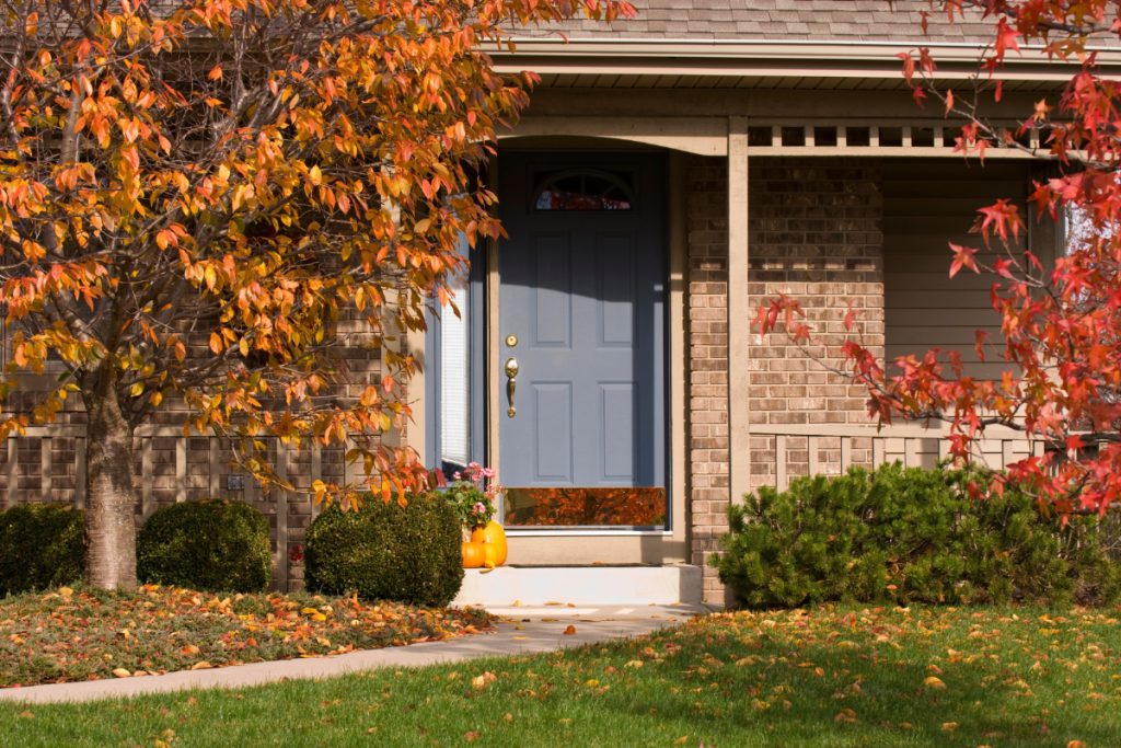 Close-up of the front of a house and front lawn in fall with a tree that has orange leaves.