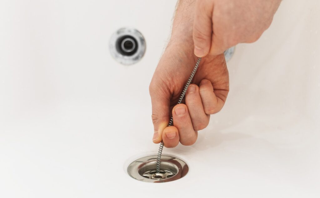 Plumber using drain auger to unclog bathtub.